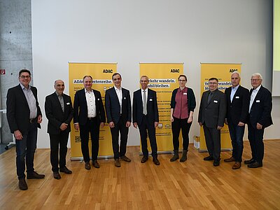 Mehrere Männer in Anzügen versammeln sich vor drei Tafeln für ein Foto im Halbkreis