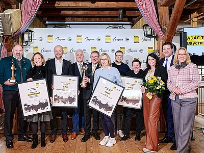 Die Gewinner des ADAC Tourismuspreis Bayern stehen auf einer Bühne und halten ihre Urkunden in den Händen